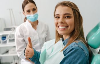 Young woman in a dental chair with perfect smile showing her thumb up