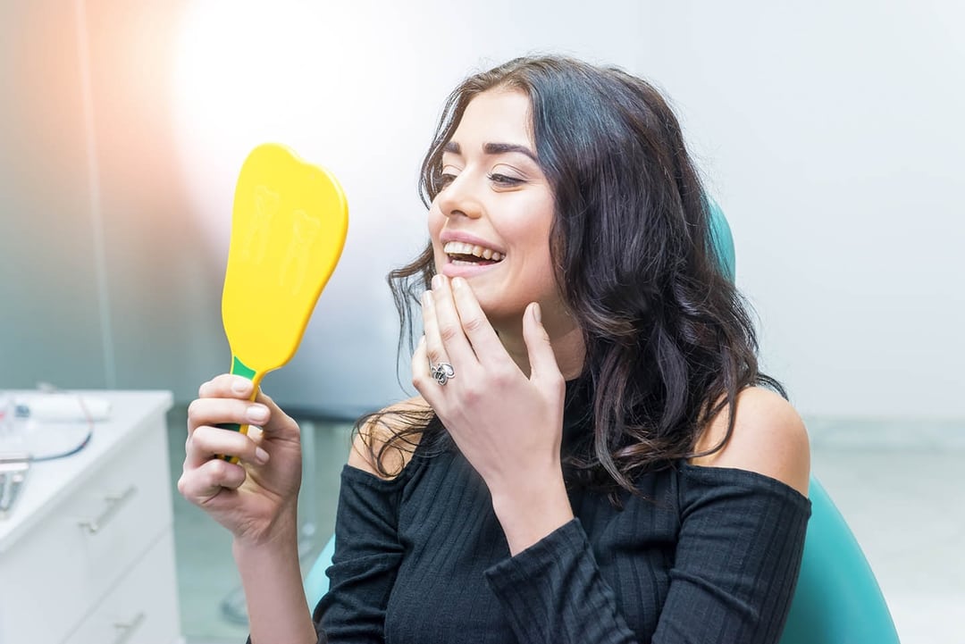 Picture of a woman checking her teeth in handheld mirror