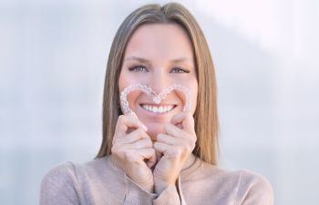 Woman with a perfect smile holding clear aligners formed in a shape of heart.